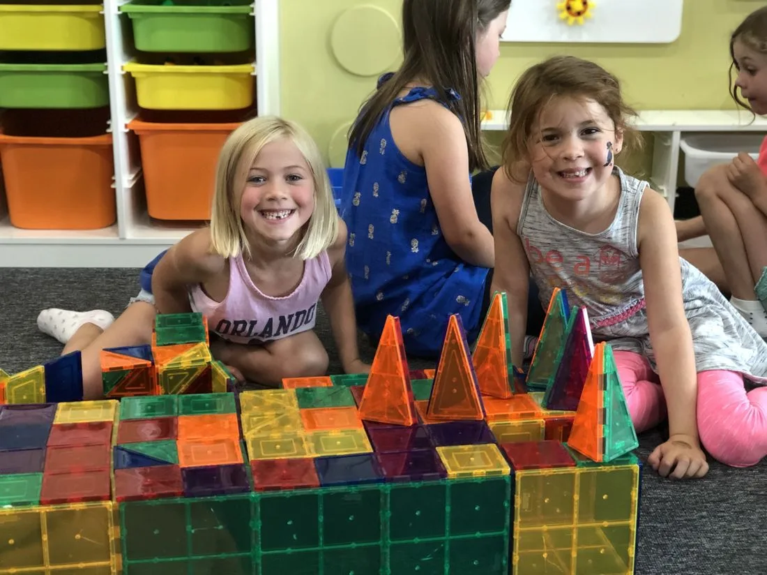 Students smiling behind a colourful Magna-Tiles castle they built together