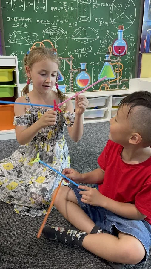 Students building with connector rods in front of a science-themed chalkboard mural